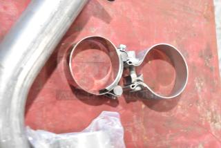 8 various exhaust pieces including clamps on a red surface. Items appear new, made of stainless steel.