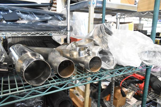 Eight various exhaust pieces on a metal shelf, including polished metal pipes and clamps, in used condition.