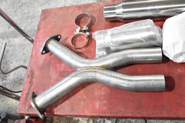 8 various exhaust pieces, including Y-pipe and clamps, on a red surface. Items appear in good condition.