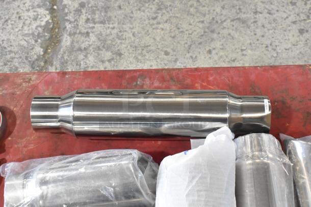 Shiny metal exhaust parts on a red surface, wrapped in plastic, showing no visible wear.