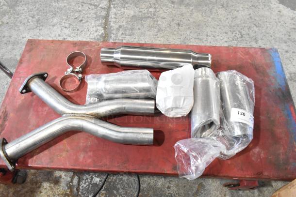Eight exhaust pieces on a red table; includes pipes, clamps, and wrapped parts. Appears unused, labeled with "130."