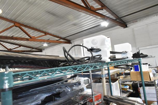 Auction items on a shelf, including a 23376474 spoiler in packaging. Industrial setting with metal beams and fluorescent lighting.