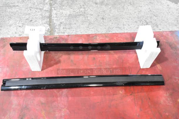 Two black spoilers with glossy finish, item number 23376474, in pristine condition, displayed with white stands on red surface.
