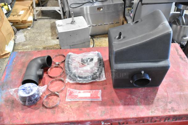 Box of parts, including a black plastic housing, elbow pipe, hose clamps, and sealed components. New condition.