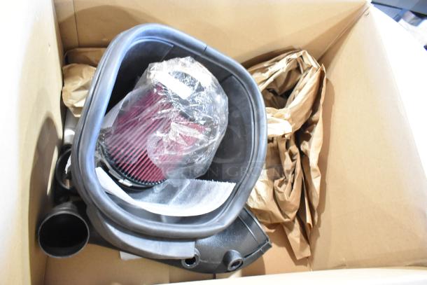 Box with assorted parts including a new red air filter in protective plastic, surrounded by packaging material.