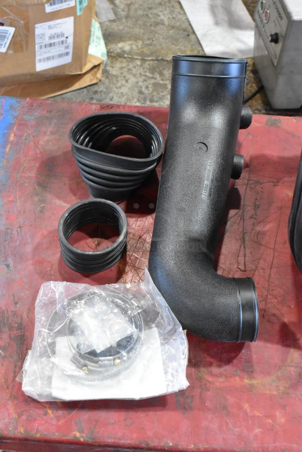 Box of automotive parts including hoses, a filter wrapped in plastic, and a black L-shaped tube on a red surface.