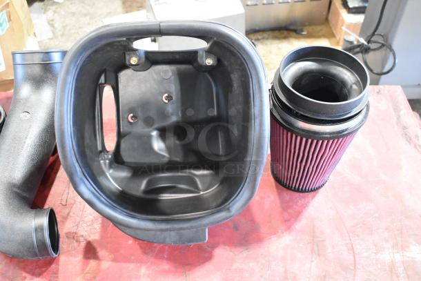 Box of parts including a cylindrical air filter and intake system components, in good condition on a workshop table.