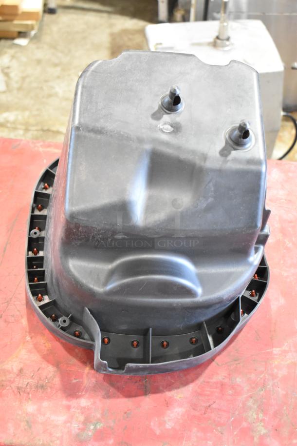 Box of parts featuring a black plastic housing component for a filter, in good condition, resting on a red surface.
