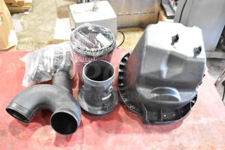 Box of car parts including a cylindrical air filter, black plastic intake manifolds, and a housing cover, in good condition.