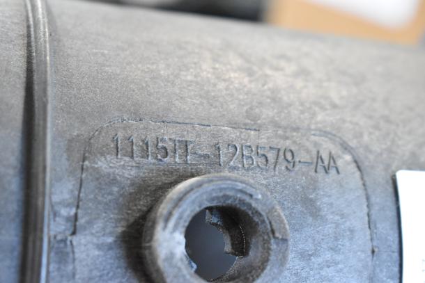 Close-up of a part with the marking "1115T-12B579-AA" embossed on its surface.