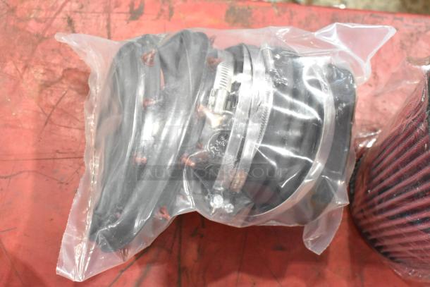 Box of parts with a filter in plastic packaging, featuring hoses and clamps, on a red background.
