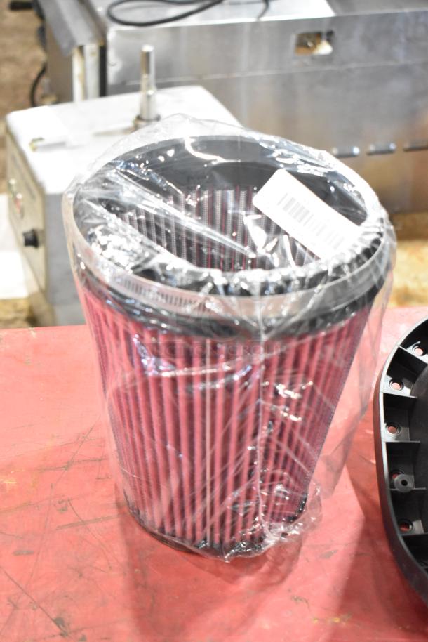 Box of parts featuring a new, wrapped cylindrical air filter with pink pleats and a black top, barcoded label visible.
