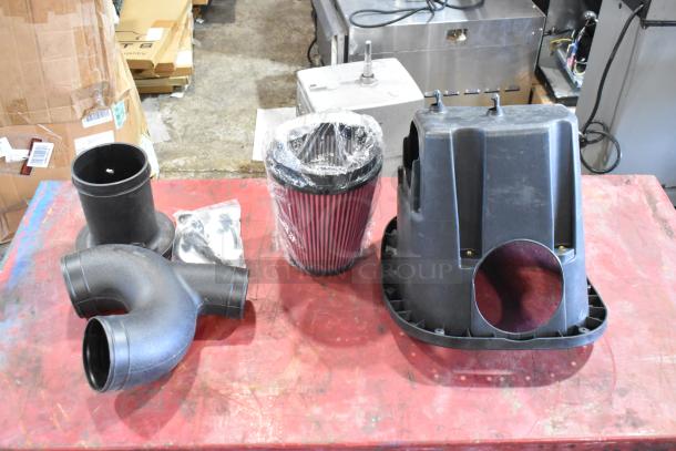 Box of parts including a red pleated filter, plastic housings, and connectors on a red table, in good condition.
