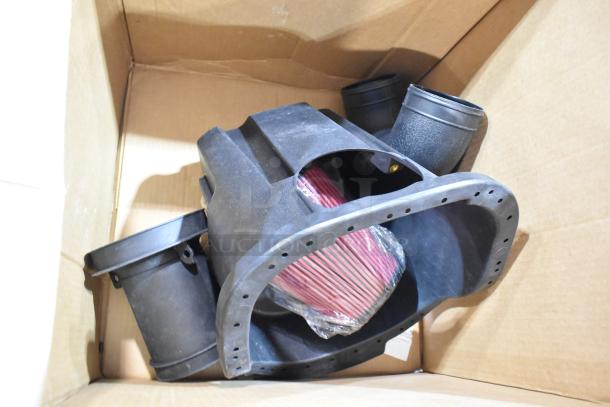 Box of automotive parts with a red air filter and black plastic components, in used condition, inside a cardboard box.