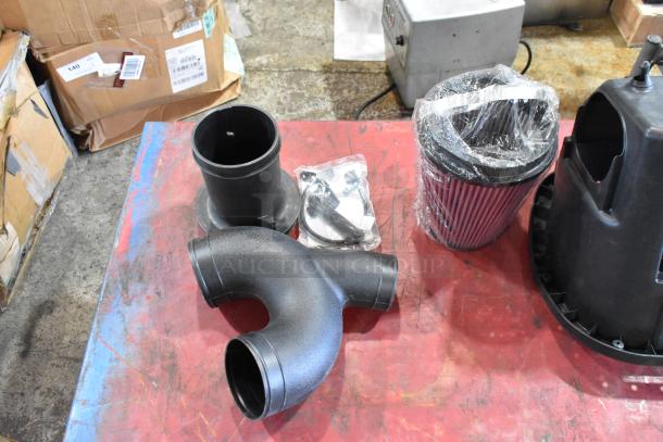 Box of mechanical parts including a sealed air filter, plastic components, and hardware, placed on a workshop table.