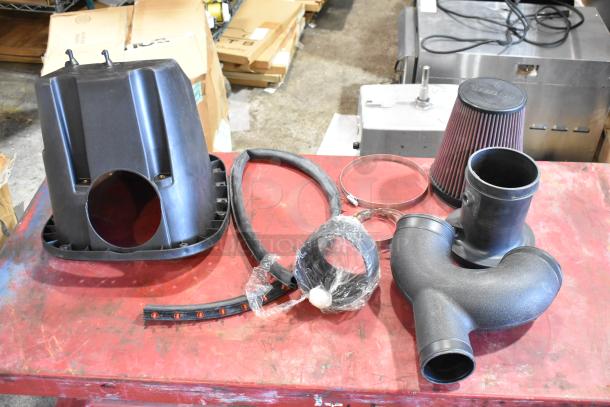 Box of automotive parts including a cold air intake kit with filter, hoses, clamps, and housing. Parts appear new.