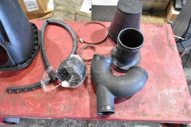 Box of parts including a cold air intake kit with filters, hoses, clamps, and components on a red surface.