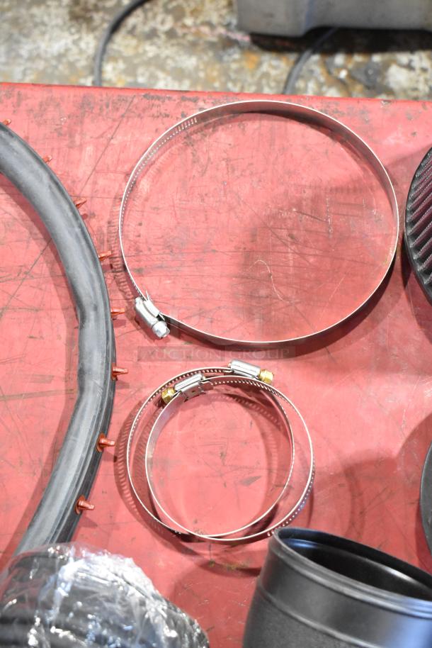 Box of automotive parts with cold air intake kit and hose clamps on red surface. Parts appear in good condition.