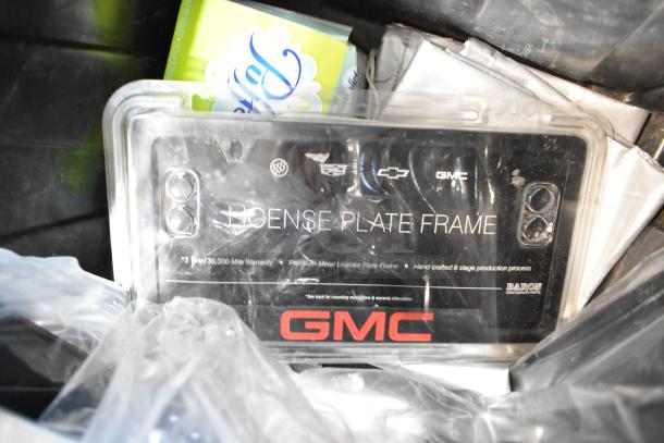 Box of parts in black poly bin, includes GMC license plate frame with 3-year warranty, and various items.