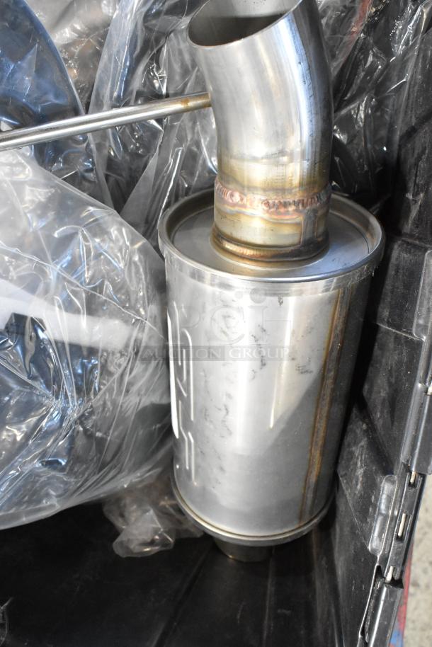 Box of automotive parts including a metal exhaust pipe, stored in a black poly bin. Parts appear new and in good condition.
