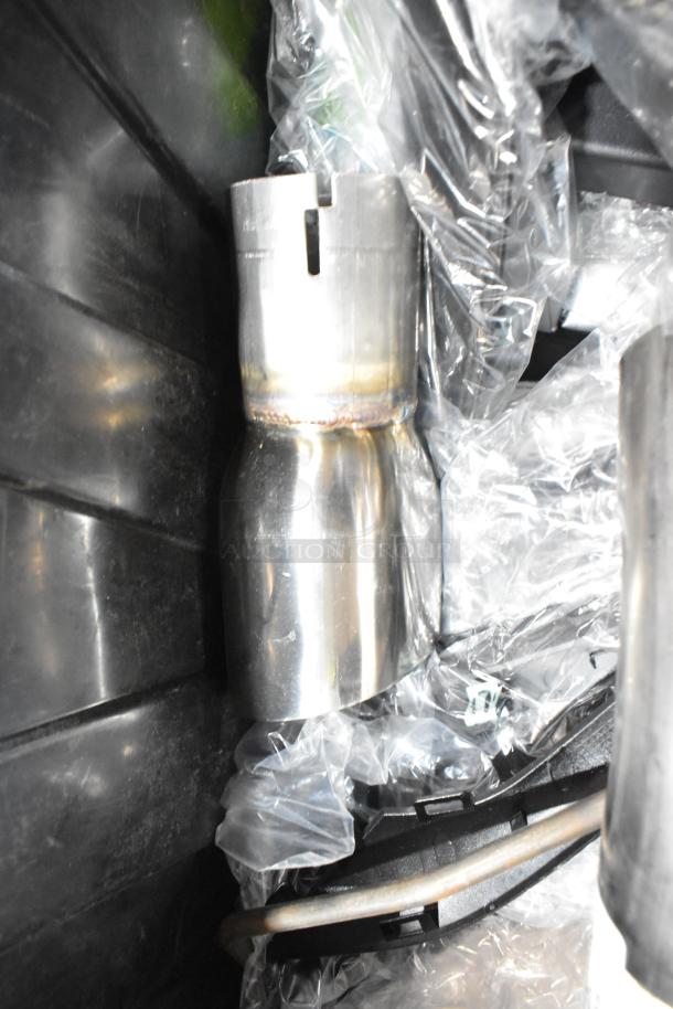 A black poly bin containing metal automotive exhaust parts and various components. Parts wrapped in protective plastic.