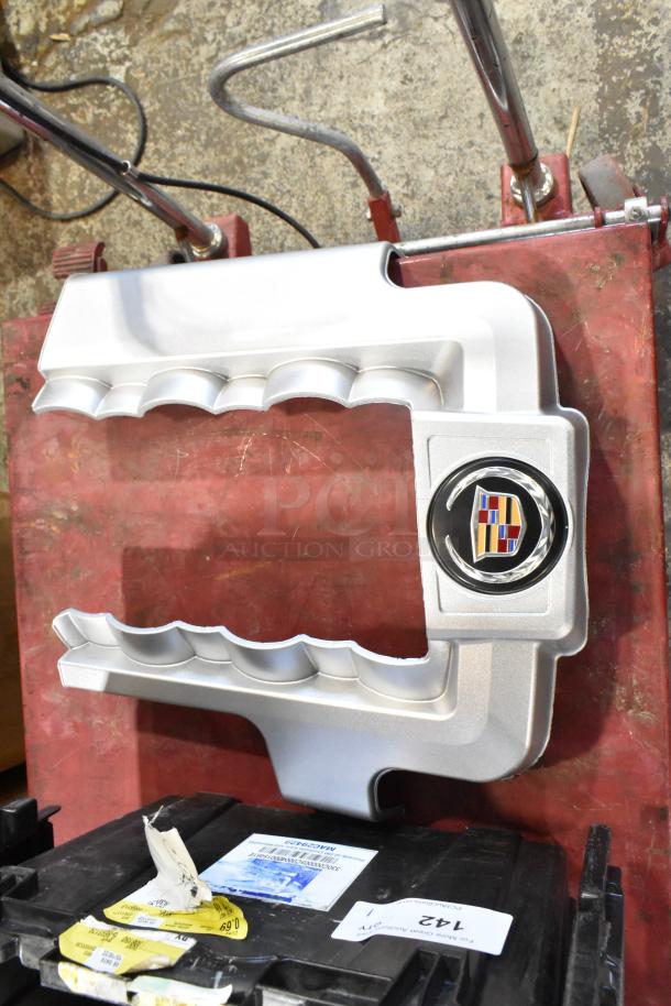 Box of parts including a silver automotive cover with a Cadillac emblem, placed in a black poly bin. Labels and tags visible.