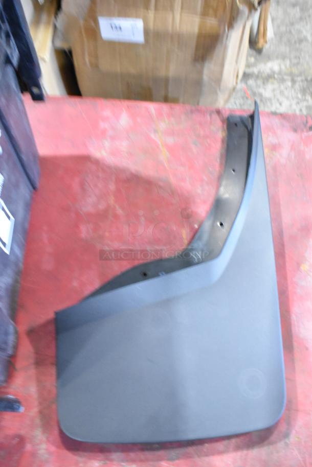 Box of GMC automotive panels in a black poly bin, showing a black panel with mounting holes on a red surface.