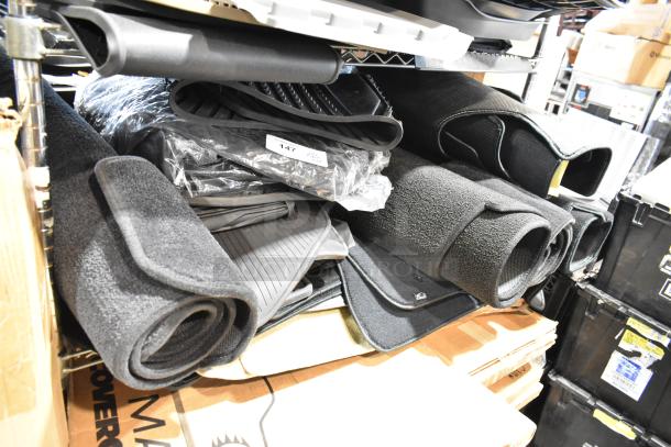 22 various car floor mats, rolled and stacked on shelves. Includes rubber and carpet types, in new condition. Lot label visible.