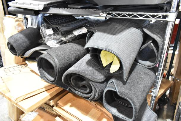 22 various car floor mats on shelf, different textures and sizes, rolled and stacked; auction lot for bid.