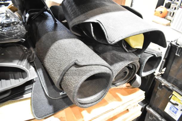 22 assorted car floor mats, rolled and stacked, in various textures and styles, indicating a bulk auction lot.