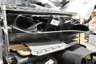 24 various car floor mats on metal shelving, mix of black and beige, new condition, lot number 148 marked.