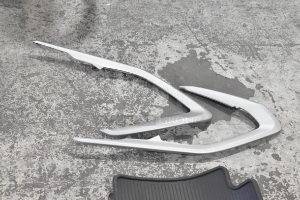 Assorted car floor mats and trim pieces on a concrete floor, featuring ribbed patterns and silver trim detailing.