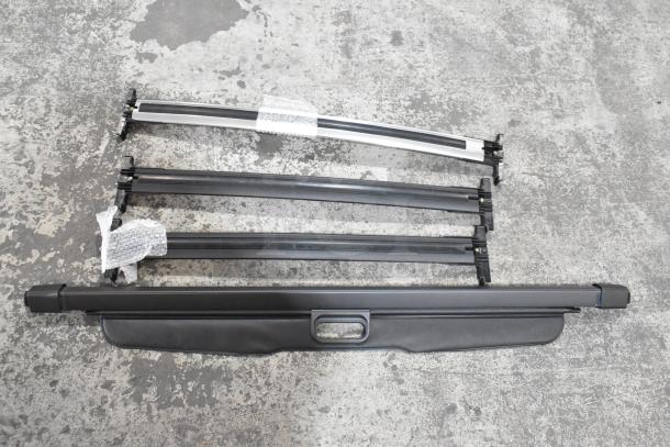 Ten automotive components including roof racks and retractable cargo cover, shown on concrete floor. Good condition.