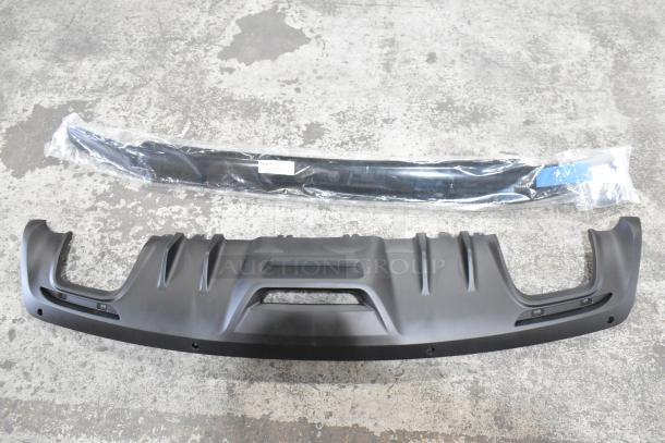 Three car accessories including a floor mat and two plastic components, one in packaging, displayed on a concrete floor.
