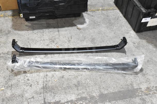 Four various items including a wrapped screen bar on the floor, in used condition, near black crates on concrete.