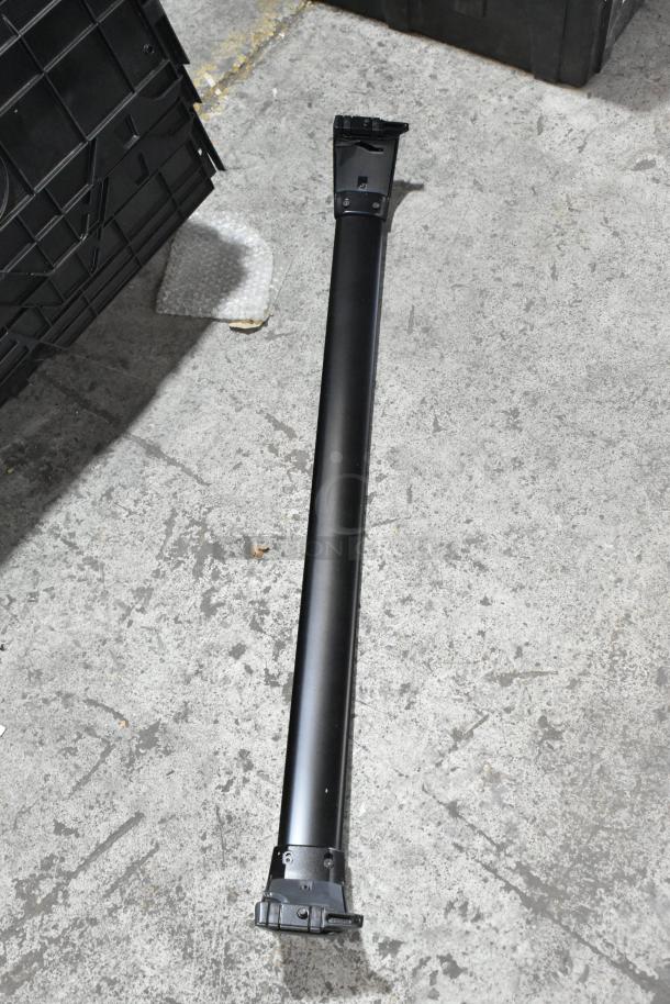 Black tubular metal component on concrete floor, used; potential part of a larger assembly, no visible markings or labels.