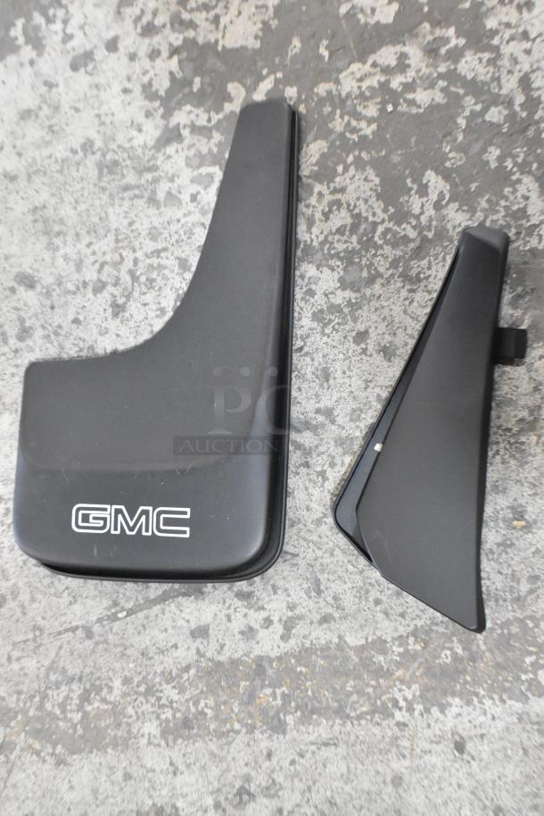 Black GMC mud flaps and panel on concrete surface, part of mixed item auction lot.