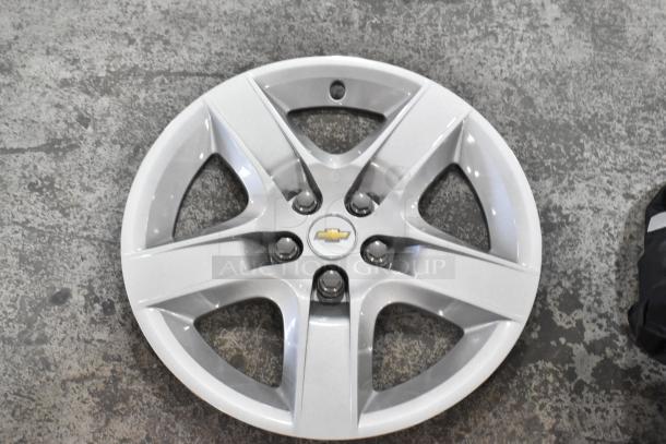 Silver Chevrolet hubcap, good condition, on concrete floor, part of diverse item auction lot.