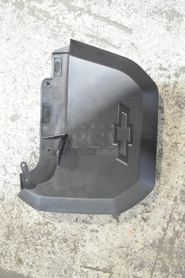 Car part with embossed Chevrolet logo on black plastic cover, in good condition on concrete surface.