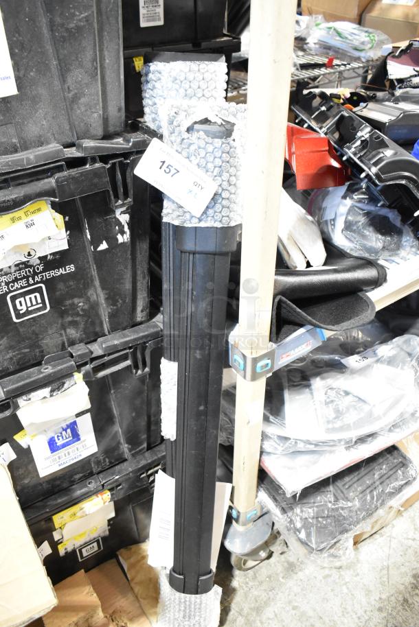 Bundle of two black tubular items wrapped in bubble wrap, labeled "157 QTY 2," against a backdrop of stacked GM storage boxes.