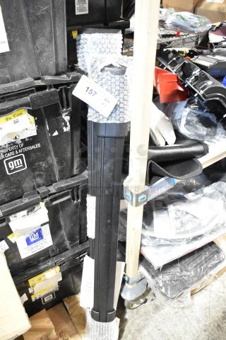 Bundle of two black tubular items wrapped in bubble wrap, labeled "157 QTY 2," against a backdrop of stacked GM storage boxes.