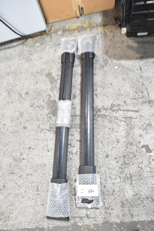 Two long black items wrapped in bubble wrap on concrete floor; tagged "157" and "2 Items. 2 Times Your Bid!"