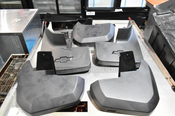 Lot of black Chevy panels with logos in a poly bin, shown on a metal surface. Various shapes, used condition.