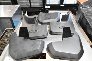 Lot of black Chevy panels with logos in a poly bin, shown on a metal surface. Various shapes, used condition.