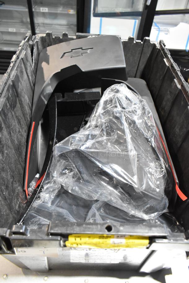 Black poly bin containing various items, including Chevy panels with emblem, some wrapped in plastic, bin shows labels.
