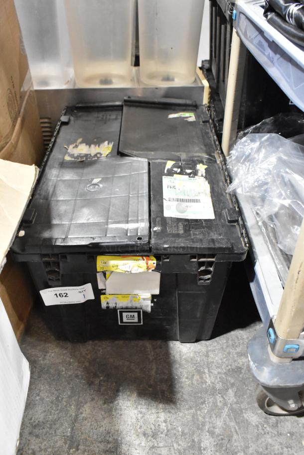 Black poly bin with GMC logo, containing various items, some labeled. Bin shows signs of wear, includes assorted materials.