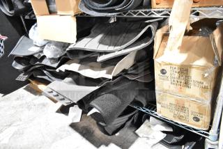 Assorted car floor mats, rubber and fabric, stacked on metal shelves with labeled Firefly boxes nearby, in mixed condition.
