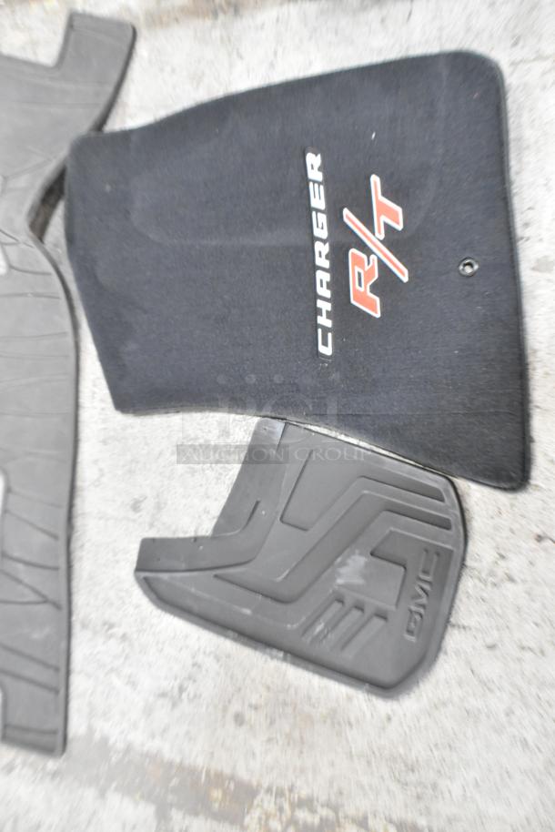 Auction lot with car floor mats, including a black Charger R/T mat and a black GMC mat. Mats show moderate wear.