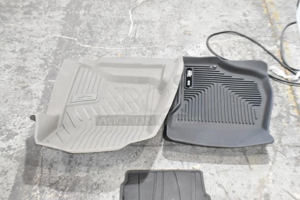 Assorted car floor mats, including a gray mat with Chevrolet logo and a black Husky Liners mat, in used condition.