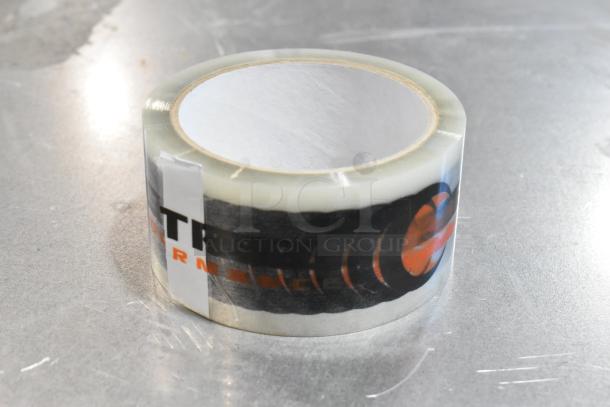 Clear packing tape roll on a metal surface, partial label with text and graphic, part of a miscellaneous auction lot.